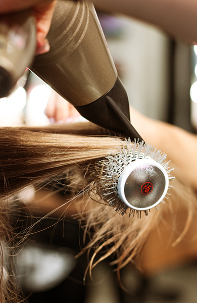 A hairstylist, with finesse, wields a hairdryer in a styling session, adding elegance to a transformative beauty journey.