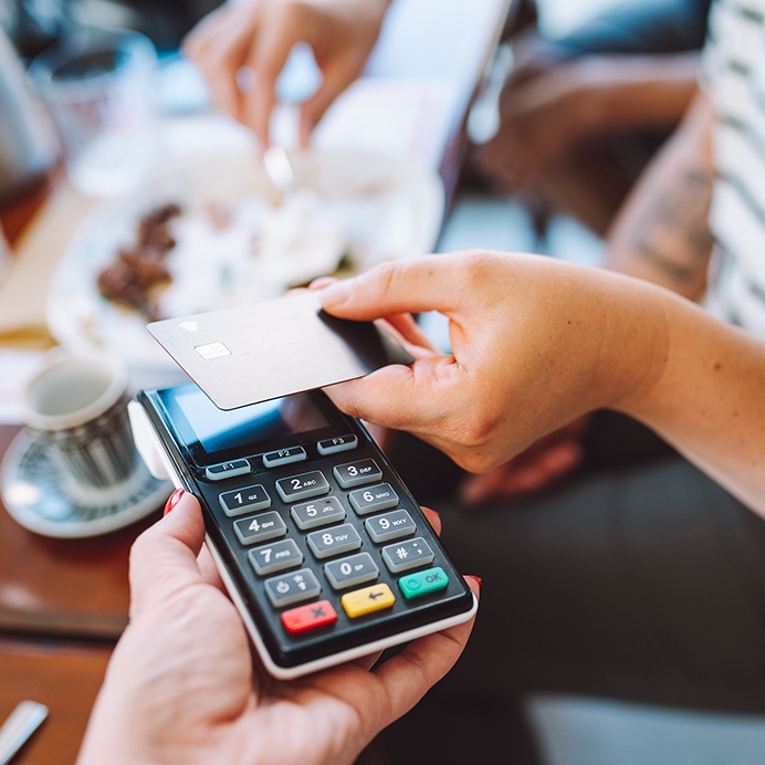 Tap to pay, cashless. Cropped woman hand holding credit card to pay in cafe for food and drinks. Focus on hand and card reader. Close up