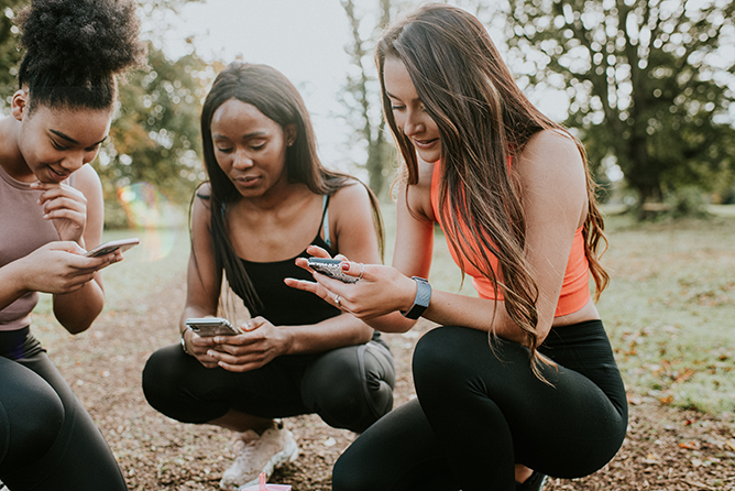Three Girls take a rest from exercising to check their phones