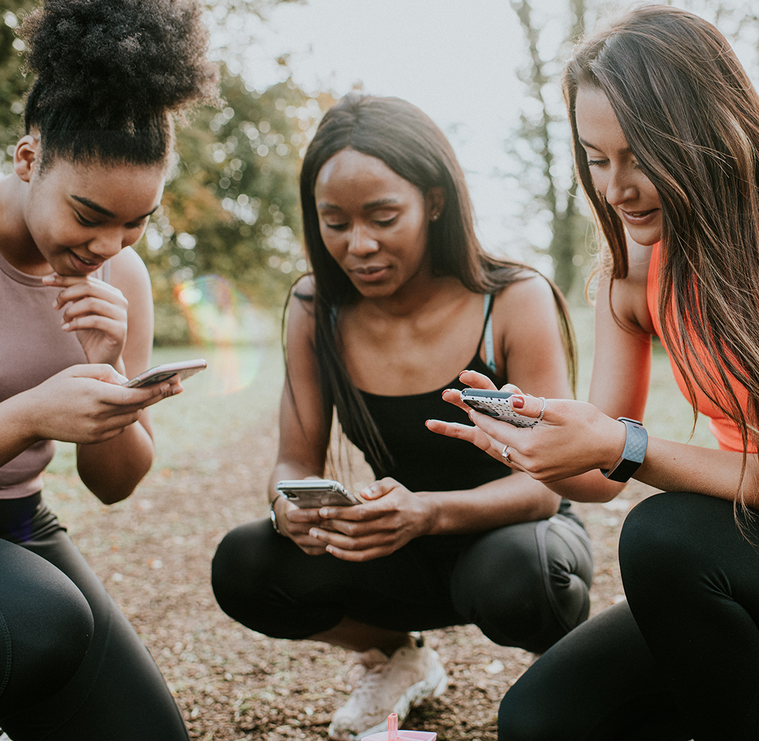 Three Girls take a rest from exercising to check their phones