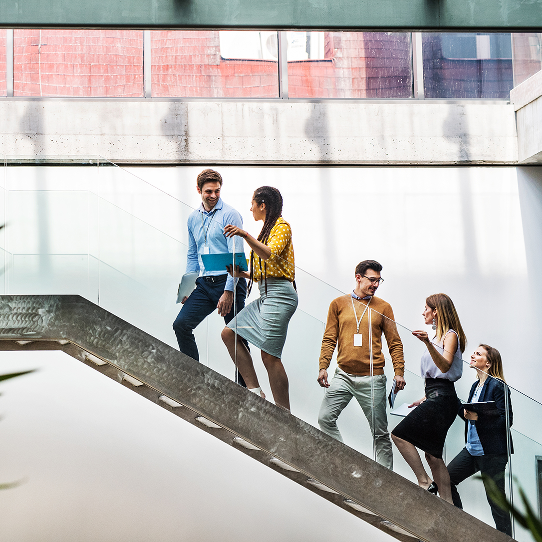 A group of businesspeople walking up the stairs in the modern building, talking.