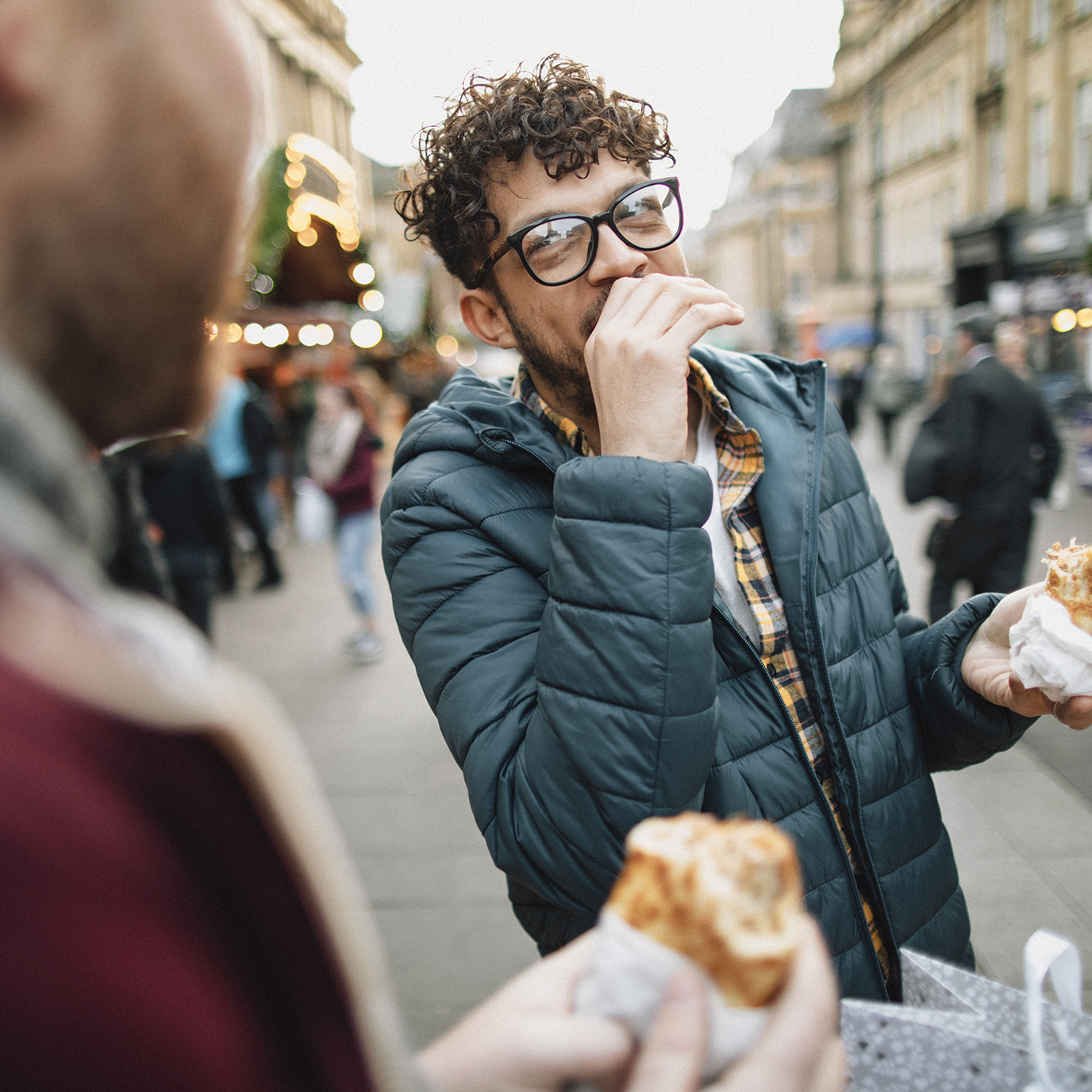 Two young gay men are eating hot food at a Christmas market.