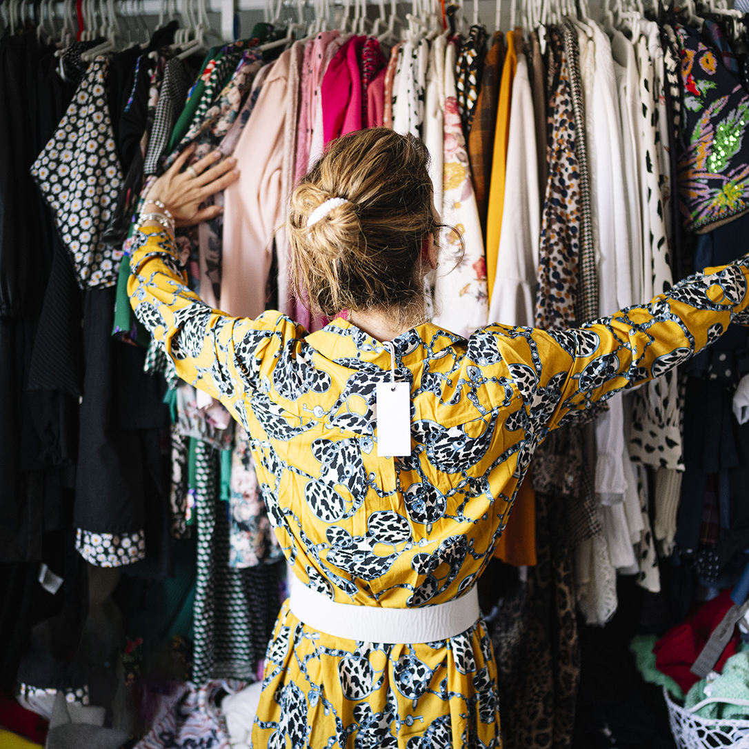 Fashionable blond woman in new yellow dress choosing from clothes rack at apartment