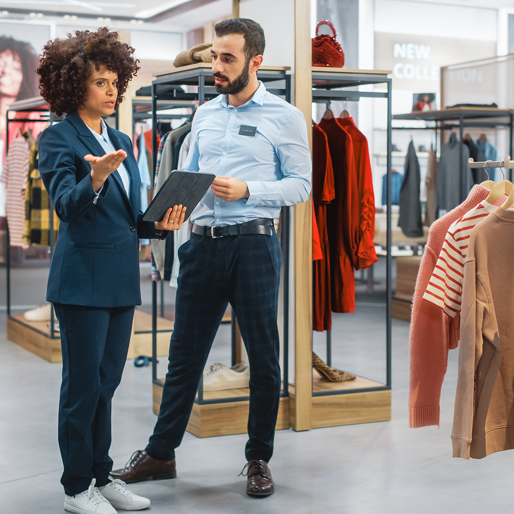 Clothing Store: Businesswoman Uses Tablet Computer, Talks to Visual Merchandising Specialist, Collaborate To Create Stylish Collection. Small Business Fashion Shop Sales Manager Talks to Designer.