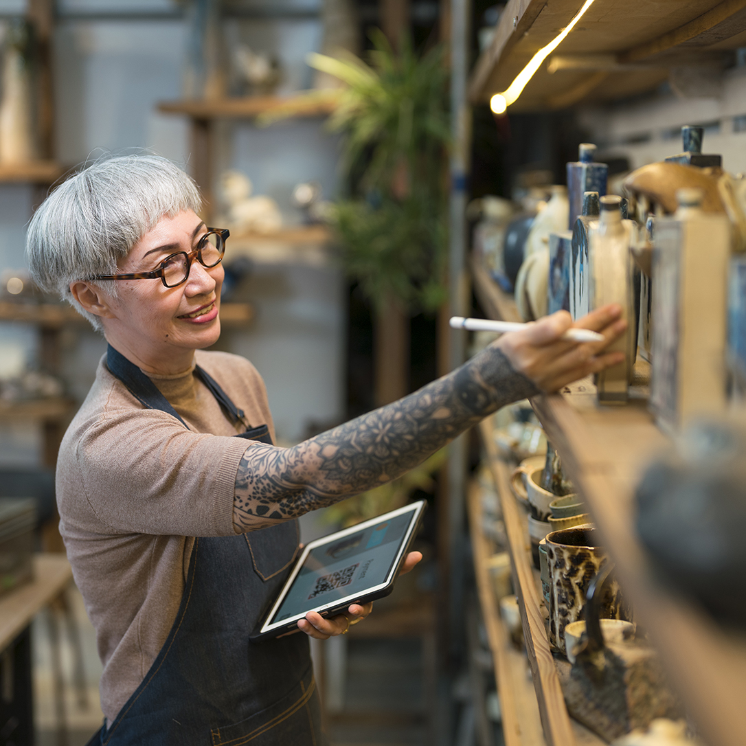 Senior artist woman using a digital tablet examining pottery in her studio.