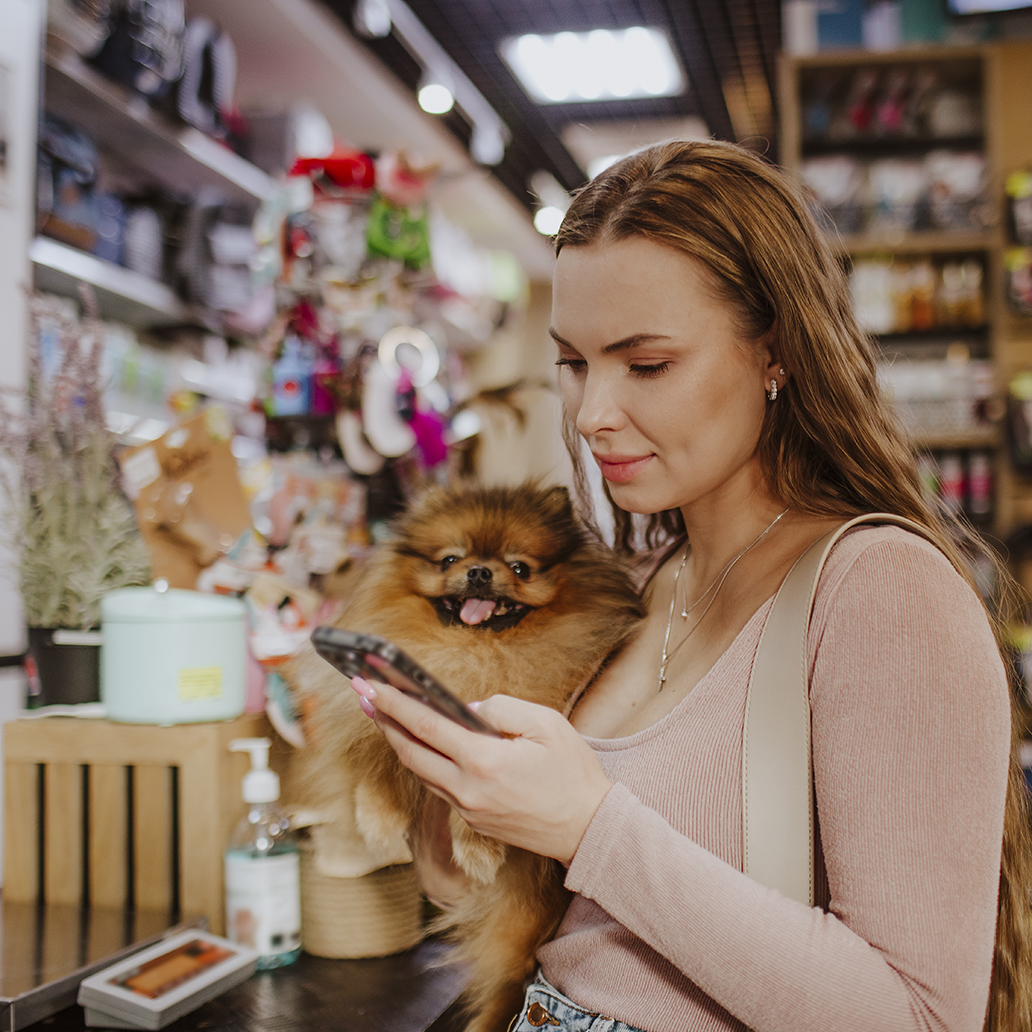 Woman carrying dog using smart phone in pet shop