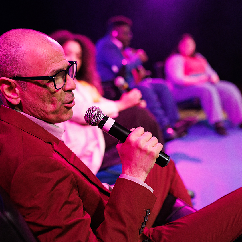 Bald man giving a speech while in the stage with other people