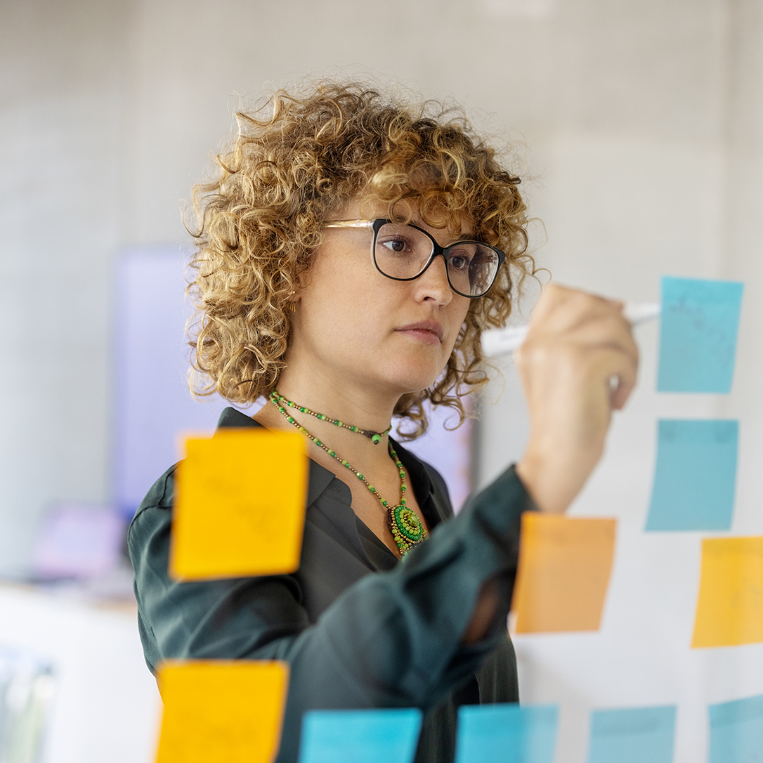 Businesswoman writing on adhesive note on glass wall at startup workplace