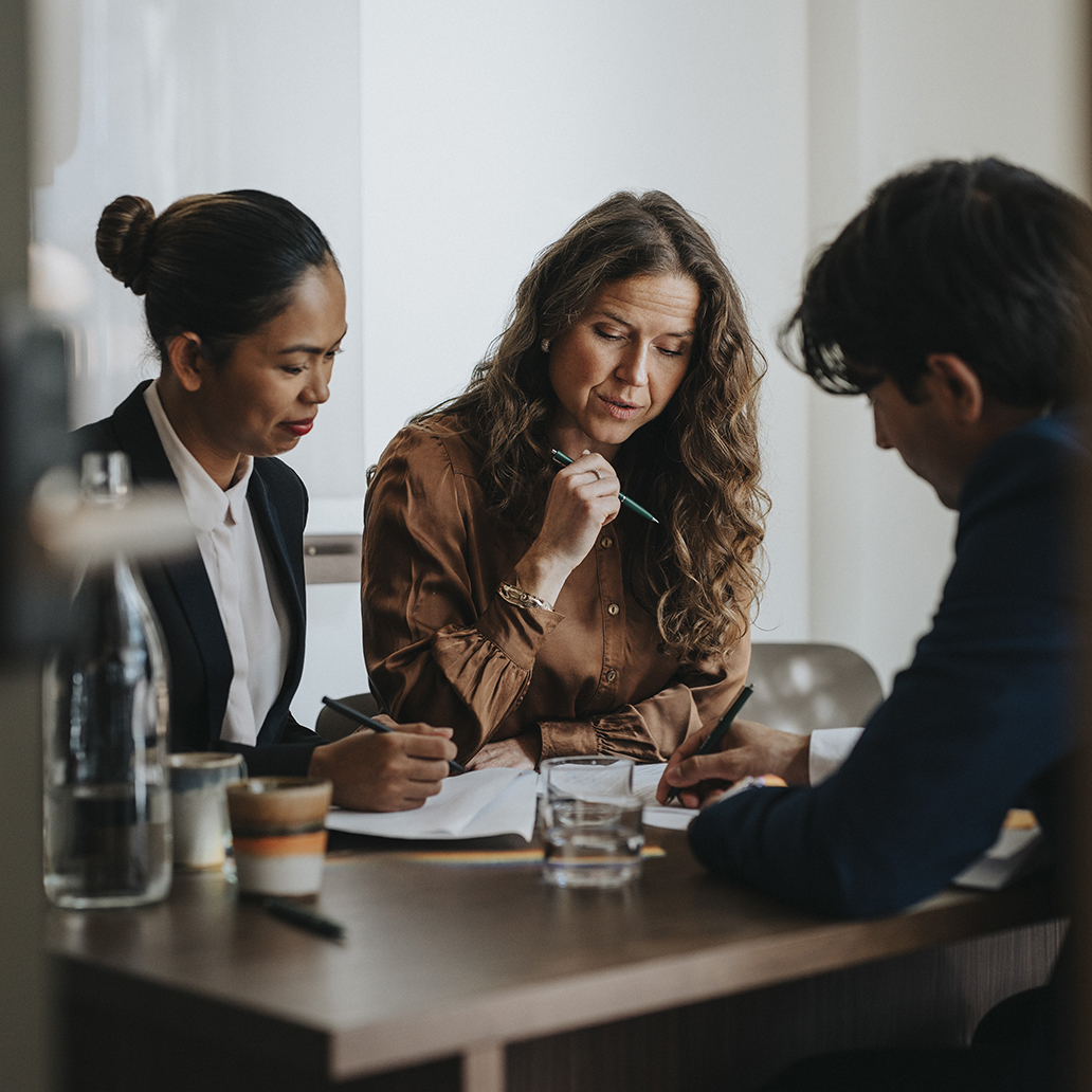 Young businessman writing while discussing strategy with female colleagues sitting at desk in office