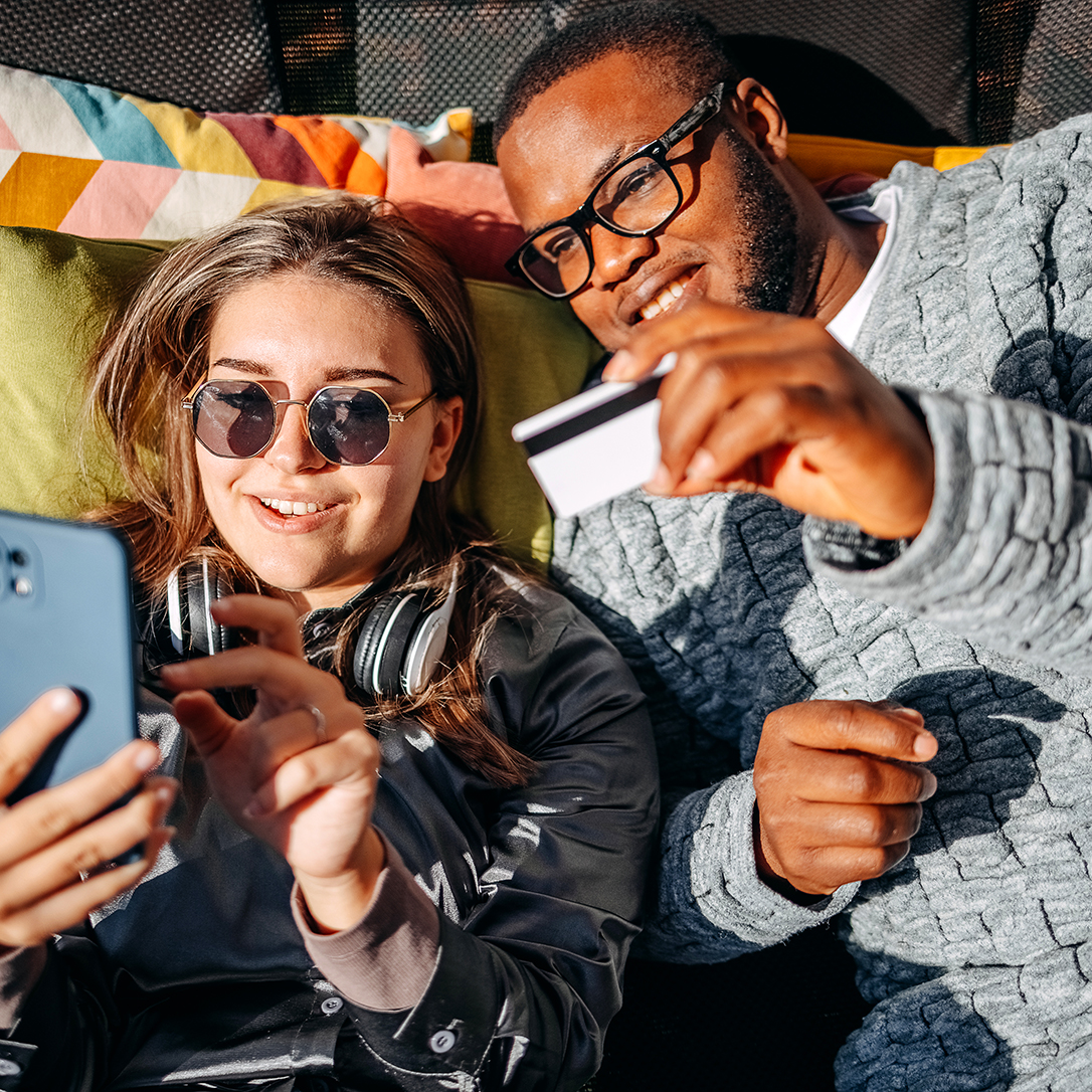 Young adults couple having fun using credit card for on line shopping at home back yard and looking at mobile phone in hand