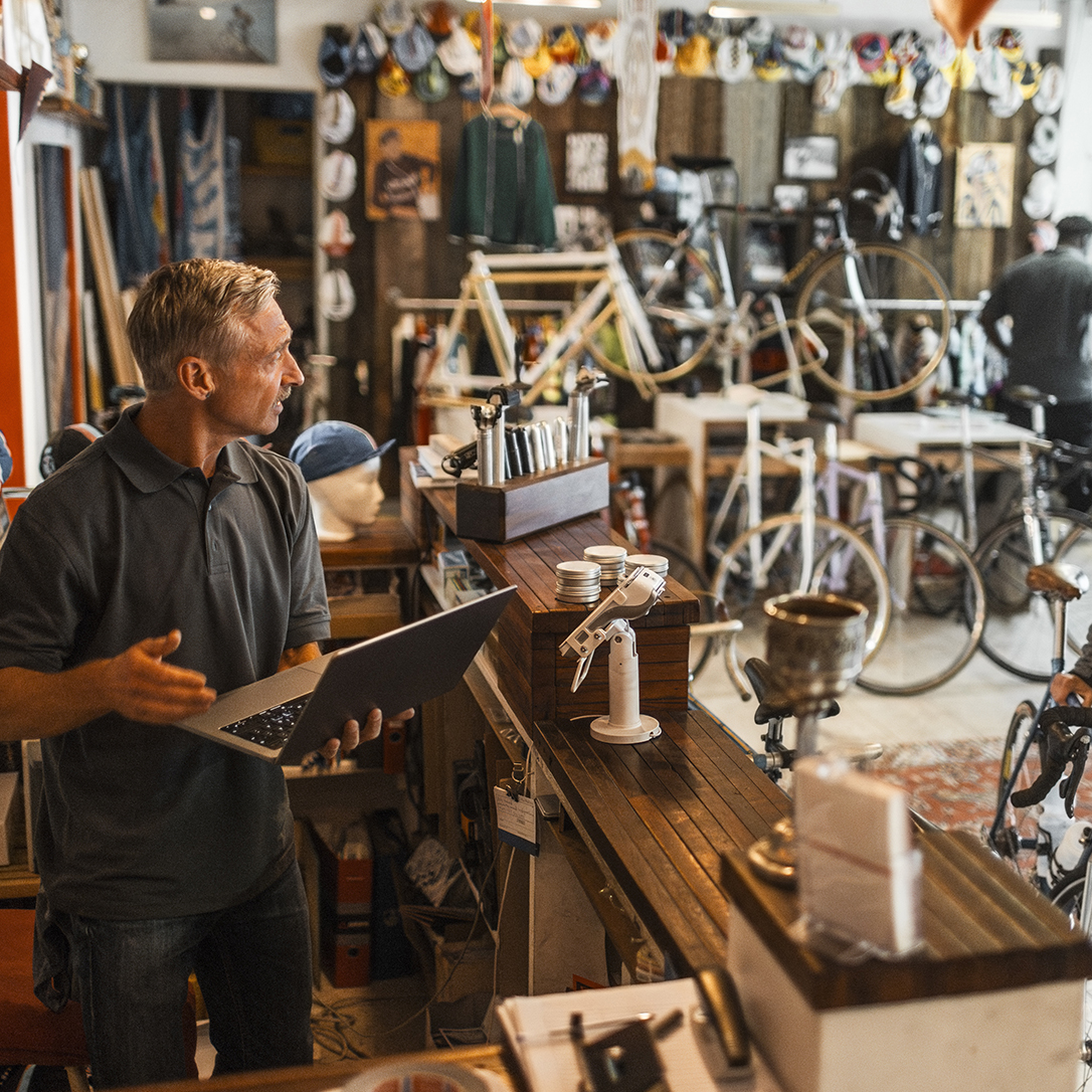 Male entrepreneur holding laptop while talking with female customer at bicycle shop