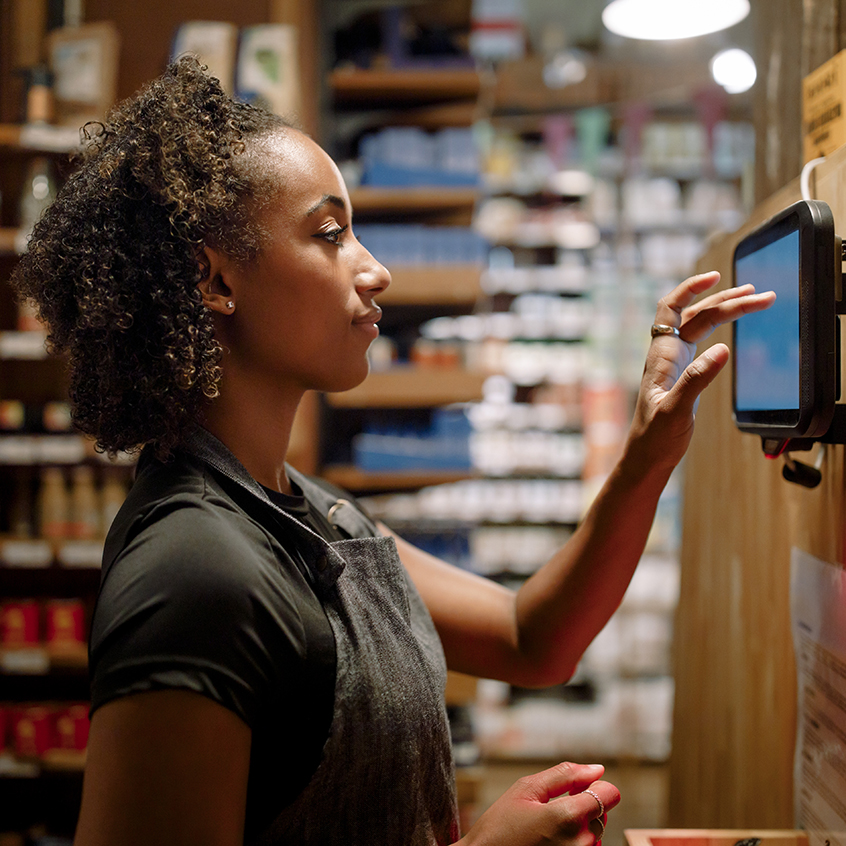 Side view of female owner using digital tablet mounted on wooden wall while working at supermarket