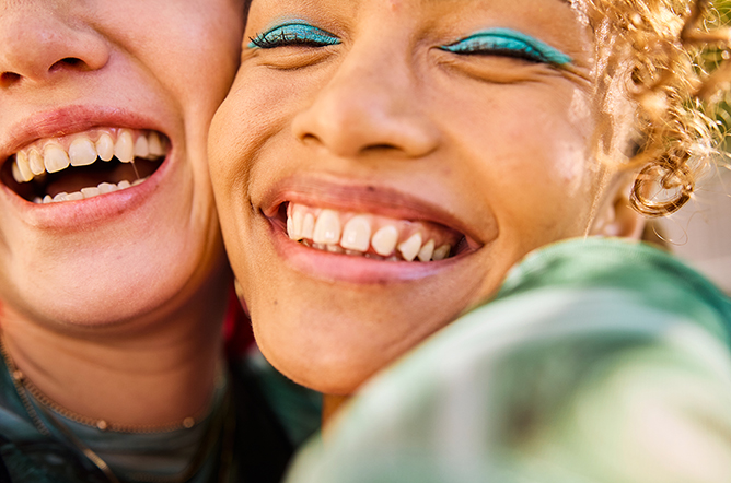 Close-up of two Gen Z adults smiling and laughing outdoors. Urban environment. Friendship and well-being.
